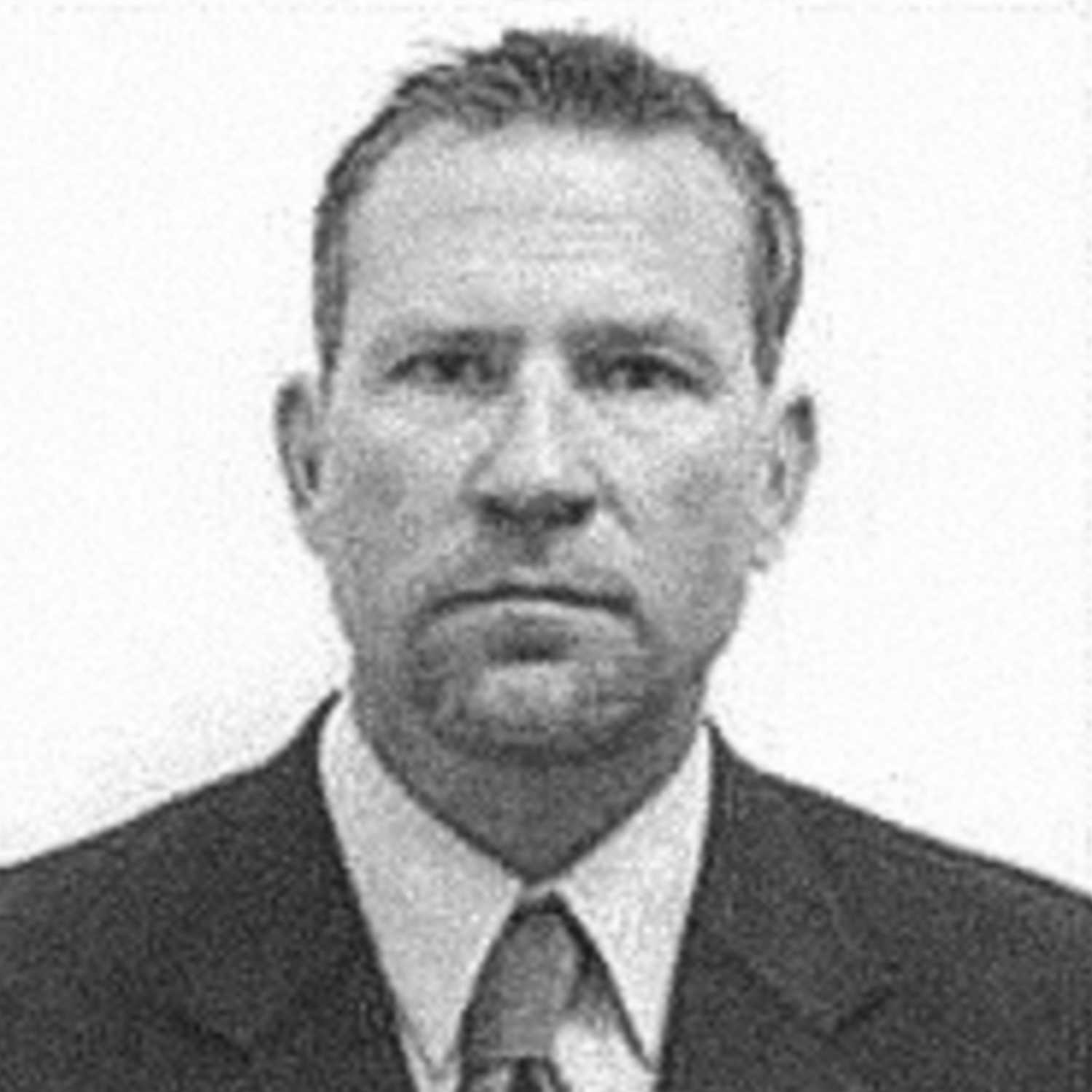 A headshot of Tyrone S. Woods, with a white backdrop, wearing a suit.